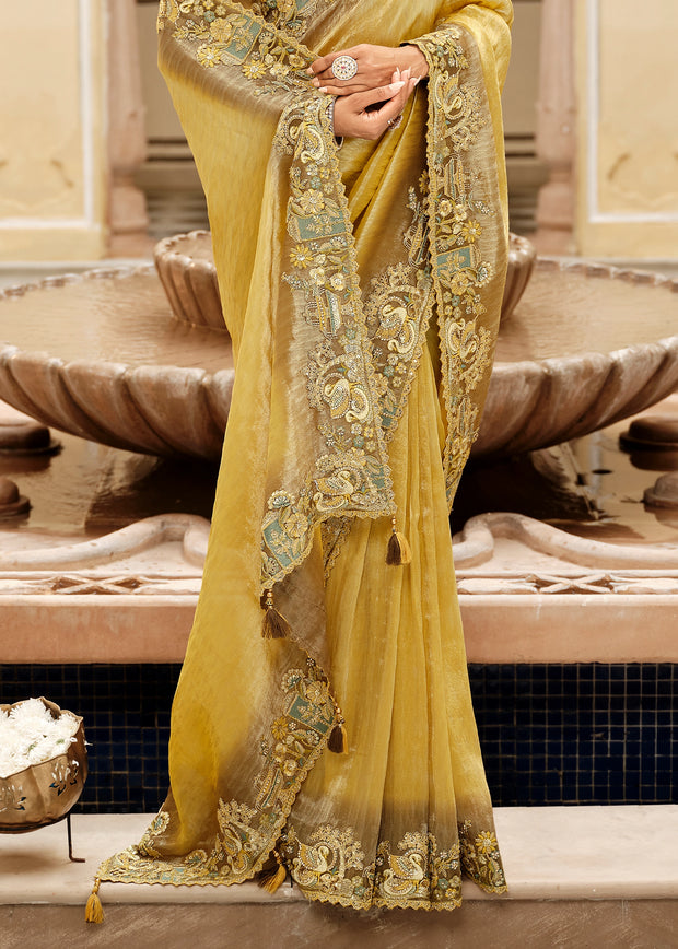 Yellow saree with intricate patterns held by a hand in front of a decorative fountain.